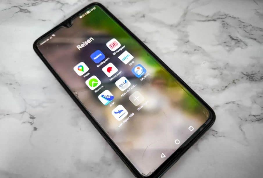 Auf einer weißen Marmorfläche liegt ein Smartphone mit einem Ordner mit der Aufschrift "Reisen" und verschiedenen reisebezogenen App-Symbolen, die die Bequemlichkeit des Reisemanagements mit nur wenigen Apps unterstreichen.