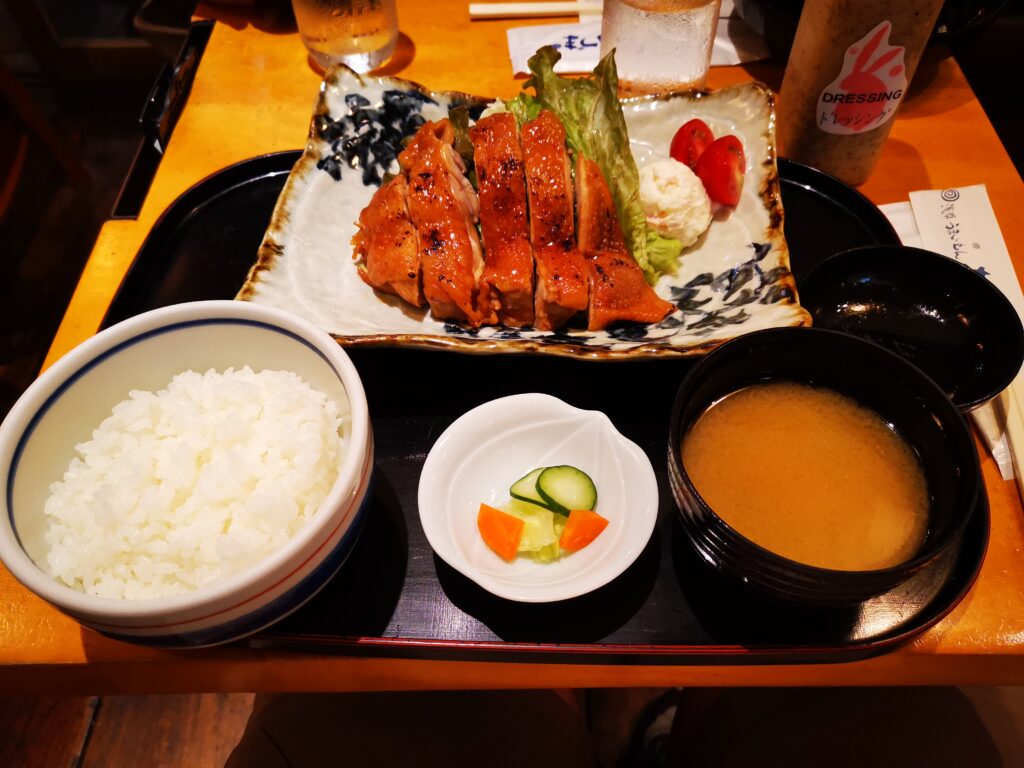 Ein japanisches Mahlzeitenset mit weißem Reis, gegrilltem Hähnchen, Kartoffelsalat, eingelegtem Gemüse und Misosuppe auf einem schwarzen Tablett - der Beweis, dass Japans Küche so viel bunter und abwechslungsreicher ist als nur Sushi. Ein echter Foodguide für Genießer!.Planen