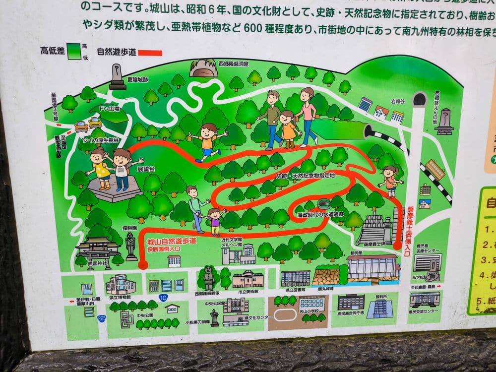 Illustrierte Karte eines Parks mit Bäumen, Wanderwegen und Cartoon-Wanderern. Gebäude, Wahrzeichen wie die Aussichtsplattform des Shiroyama-Parks und Wege sind auf Japanisch beschriftet. Eine rote Linie markiert eine vorgeschlagene Route mit Blick auf Sakurajima. Shiroyama Park Observation Deck in Kagoshima