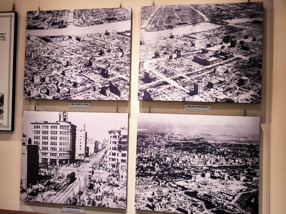 Vier Schwarz-Weiß-Luftaufnahmen einer Stadt nach dem Großen Kanto-Erdbeben sind an einer Wand ausgestellt und zeigen beschädigte Gebäude und leere Straßen. Zu den Luftbildern in dieser Ausstellung des Memorial Museums gehört auch ein Foto auf Straßenebene.