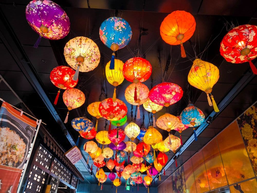 Bunte Papierlaternen mit Blumenmustern hängen von der dunklen Decke und sorgen für eine lebendige und festliche Atmosphäre, die an die lebhaften Feste in Enoshima erinnert.