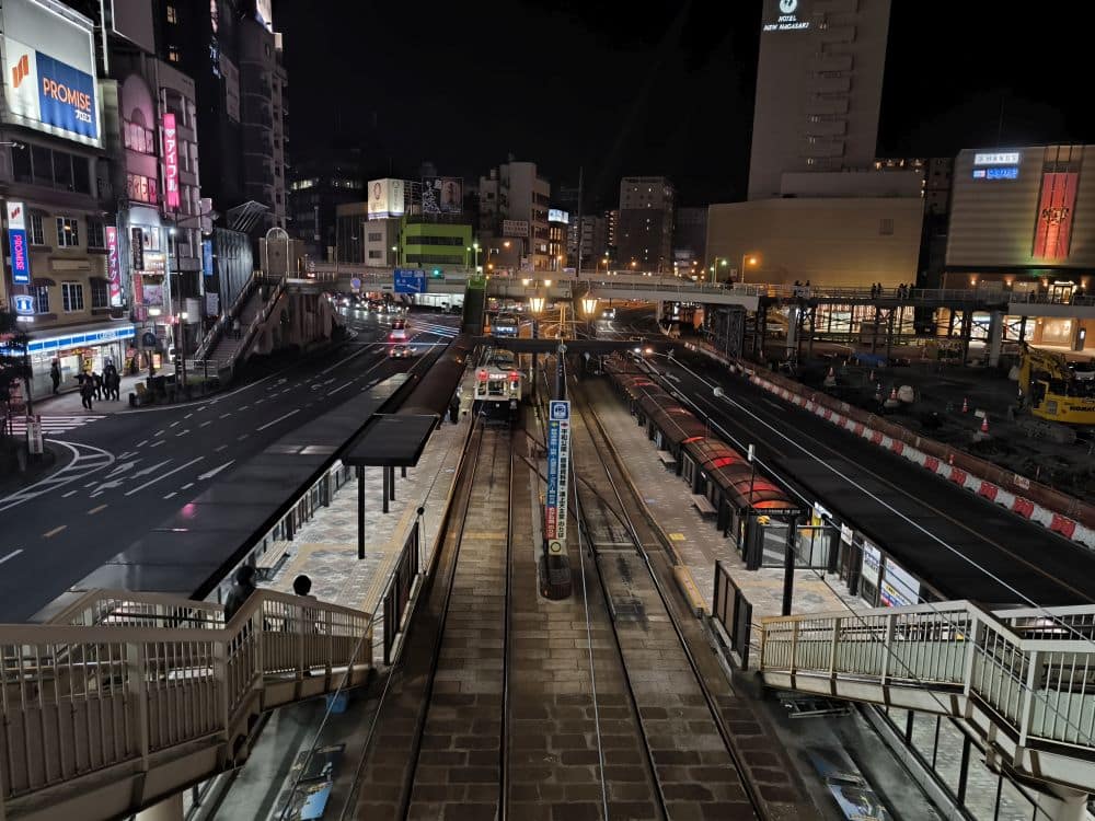 Nachtansicht einer Straßenbahnhaltestelle von oben, mit leeren Bahnsteigen und beleuchteten Straßen - perfekt für alle, die sich von Tramreisen Nagasaki inspirieren lassen wollen oder Tipps suchen, wie man am besten mit der Straßenbahn durch Nagasaki bei Nacht fährt.