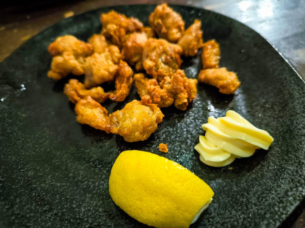 Ein dunkler Teller mit mehreren Stücken gebratenem Hino-Huhn, einem Klecks Mayonnaise und einer Zitronenspalte an der Seite.