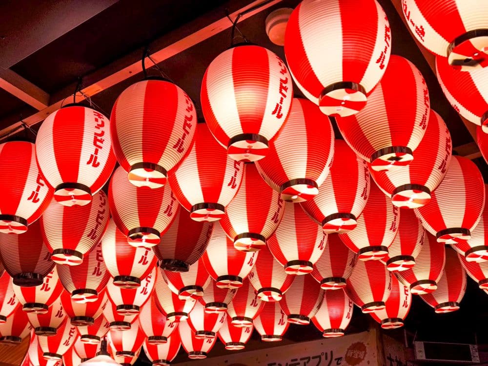 Reihen von roten und weißen japanischen Papierlaternen mit vertikaler Schrift hängen in Kawagoe von der Decke, leuchten warm und schaffen eine festliche Atmosphäre.