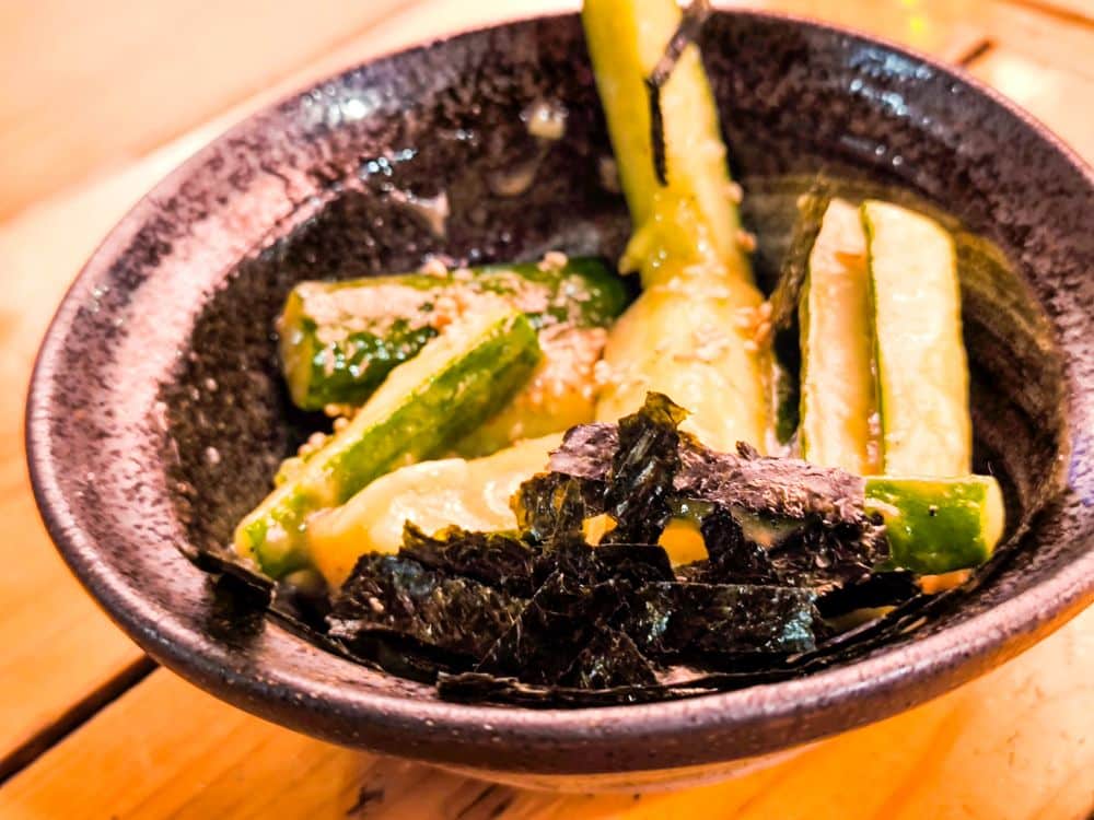 Eine schwarze Schale mit geschnittenen Gurken, Sesam, Soße und Seetangstreifen steht auf einem Holztisch in Kawagoe.