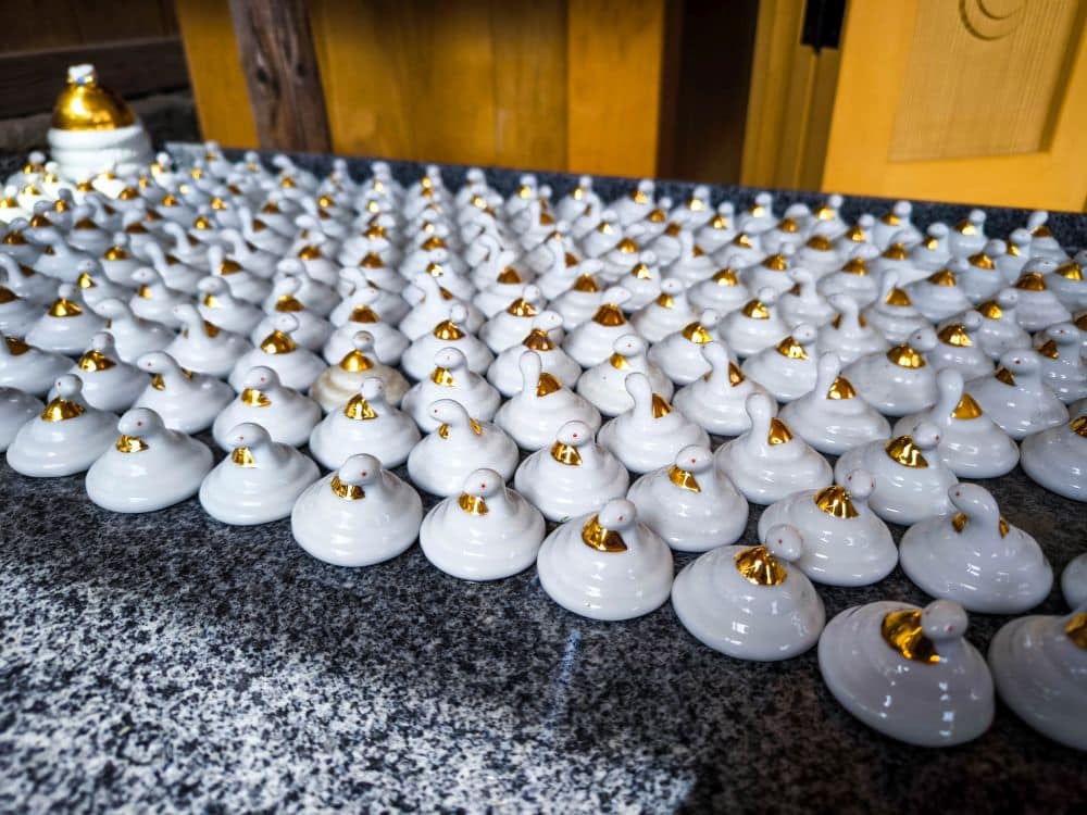 Auf einer grau gesprenkelten Arbeitsplatte stehen reihenweise kleine, weiße Keramikbehälter mit goldenen Deckeln, die an den raffinierten Minimalismus von Kawagoe erinnern, wobei ein etwas anderer Behälter in der hinteren Ecke steht.