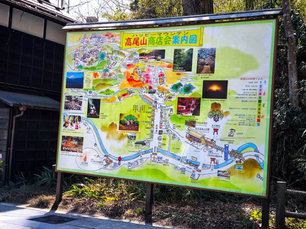 Eine farbenfrohe illustrierte Karte des Berges Takao in Japan mit Wanderwegen, Sehenswürdigkeiten, Fotos und Points of Interest, die im Freien neben einem Gebäude und inmitten von Grünflächen in der Nähe von Takao aufgestellt ist.