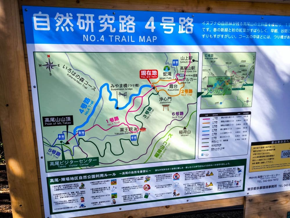 Foto einer farbenfrohen Wanderkarte mit dem Titel No. 4 Trail Map in Japanisch und Englisch, die Wanderrouten, Sehenswürdigkeiten und Rastplätze rund um den Berg Takao zeigt, mit einer "Sie sind hier"-Markierung, hilfreichen Hinweisen und Informationssymbolen.