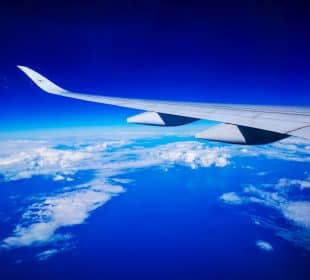 Bewundern Sie die atemberaubende Aussicht von Ihrem Sitzplatz auf Flüge nach Japan - ein Flugzeugflügel, der über weißen Wolken, tiefblauem Himmel und dem Horizont der Erde schwebt, verspricht Abenteuer in Japan.