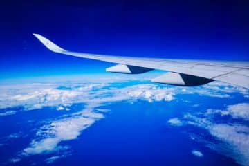 Bewundern Sie die atemberaubende Aussicht von Ihrem Sitzplatz auf Flüge nach Japan - ein Flugzeugflügel, der über weißen Wolken, tiefblauem Himmel und dem Horizont der Erde schwebt, verspricht Abenteuer in Japan.