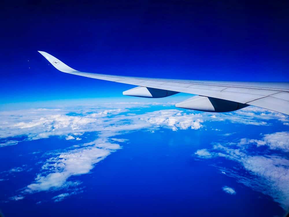Bewundern Sie die atemberaubende Aussicht von Ihrem Sitzplatz auf Flüge nach Japan - ein Flugzeugflügel, der über weißen Wolken, tiefblauem Himmel und dem Horizont der Erde schwebt, verspricht Abenteuer in Japan.