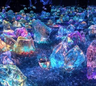 Große, farbenfrohe Kristalle und Felsen leuchten in kräftigem Blau, Rosa, Lila und Grün und schaffen eine magische Landschaft, die an das TeamLab Biovortex Kyoto erinnert - eine Verschmelzung von Technologie und Kunst in einer leuchtenden Sci-Fi-Fantasiewelt.