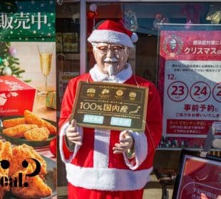Eine lebensgroße Colonel-Sanders-Statue als Weihnachtsmann verkleidet steht vor einem KFC in Japan und hält ein Schild in Japanisch. Weihnachtsdekoration und Werbung für Brathähnchengerichte unterstreichen die Tradition des japanischen Weihnachtsessens bei KFC.