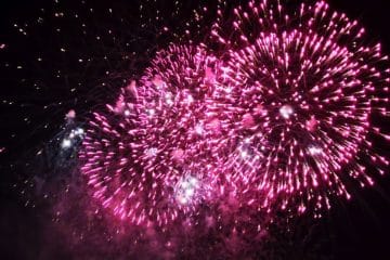 Leuchtend rosafarbene Feuerwerkskörper japanischer Art explodieren vor dem dunklen Nachthimmel, in der Mitte funkelnde weiße Lichterbüschel - ein inspirierendes Feuerwerk zur Feier von Neuanfang und Akemashite Omedetou.