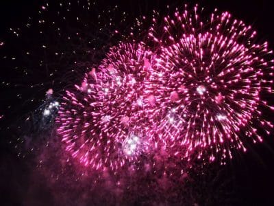 Leuchtend rosafarbene Feuerwerkskörper japanischer Art explodieren vor dem dunklen Nachthimmel, in der Mitte funkelnde weiße Lichterbüschel - ein inspirierendes Feuerwerk zur Feier von Neuanfang und Akemashite Omedetou.
