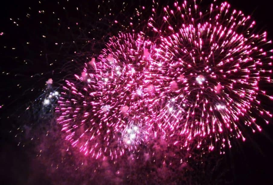 Leuchtend rosafarbene Feuerwerkskörper japanischer Art explodieren vor dem dunklen Nachthimmel, in der Mitte funkelnde weiße Lichterbüschel - ein inspirierendes Feuerwerk zur Feier von Neuanfang und Akemashite Omedetou.