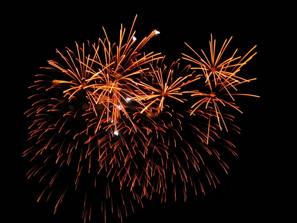 Vor dem schwarzen Nachthimmel explodiert ein orangefarbenes Feuerwerk, dessen leuchtende Schlieren nach außen strahlen - ein feierliches "Gesundes Neues Jahr" und ein strahlender Neuanfang Japan.