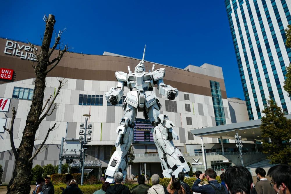 Die beeindruckende Einhorn-Gundam-Roboter-Statue thront im Freien in Odaiba, Tokio, vor der DiverCity Tokyo Plaza, während sich die Menschen unter dem klaren blauen Himmel versammeln.