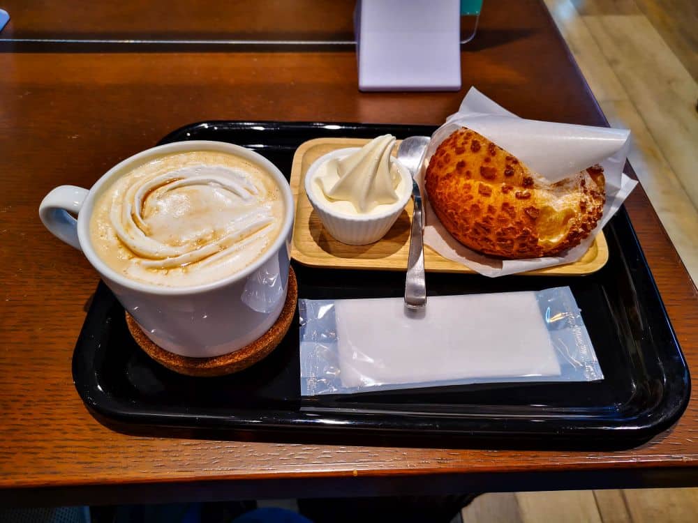 Eine Tasse Schaumkaffee, ein Schälchen Softeis mit Löffel und ein Windbeutel auf einem Tablett, das auf einem Holztisch steht - perfekt, um die Anime-Kultur und den urbanen Charme von Ikebukuro aufzusaugen.