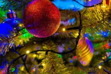 Die Nahaufnahme eines geschmückten Weihnachtsbaums fängt den Geist der Weihnacht ein: Ein roter Glitzerschmuck, goldene und silberne Kugeln und bunte Lichter sorgen für eine festliche und lebendige Weihnachtsatmosphäre.