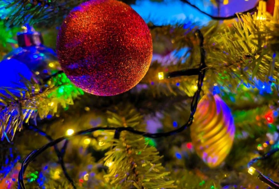 Die Nahaufnahme eines geschmückten Weihnachtsbaums fängt den Geist der Weihnacht ein: Ein roter Glitzerschmuck, goldene und silberne Kugeln und bunte Lichter sorgen für eine festliche und lebendige Weihnachtsatmosphäre.
