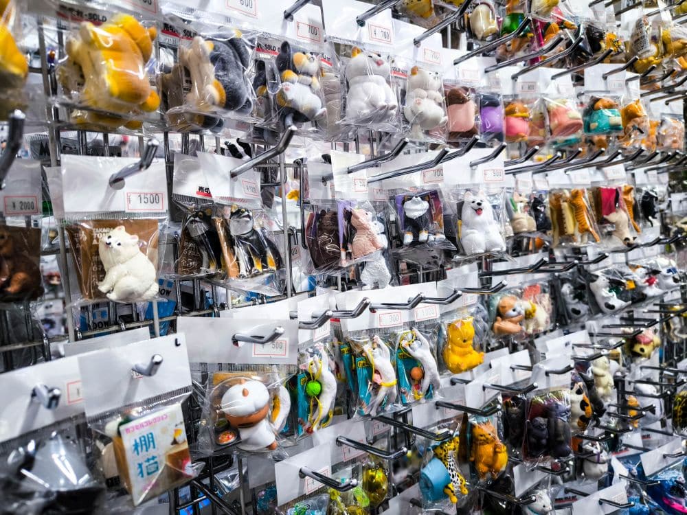 In einem Geschäft am Nakano Broadway sind zahlreiche Regale mit kleinen Tierfiguren und Schlüsselanhängern in durchsichtigen Plastikverpackungen in ordentlichen Reihen angeordnet. Über jeder Verpackung ist ein Preisschild angebracht.