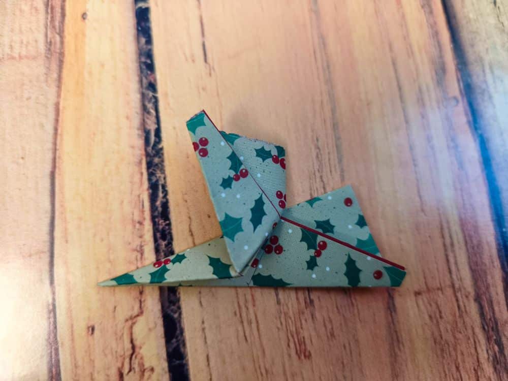 Ein Origami-Kranich aus Papier mit einem Stechpalmenmuster ruht elegant auf einer Holzfläche.