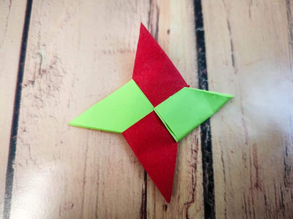 Ein Origami-Ninja-Stern mit abwechselnd roten und grünen Abschnitten ruht auf einer Holzfläche.
