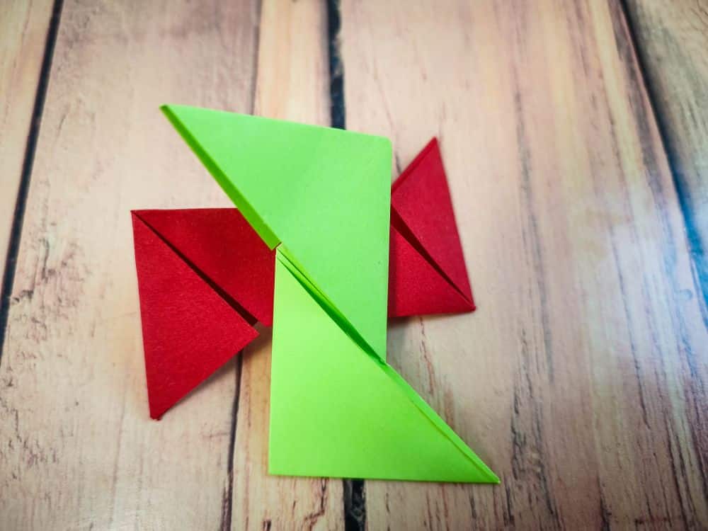 Drei bunte Origami-Dreiecke - zwei rote und ein grünes - sind auf einer Holzfläche angeordnet, wobei sich das grüne Origami-Stück mit dem roten überlappt.