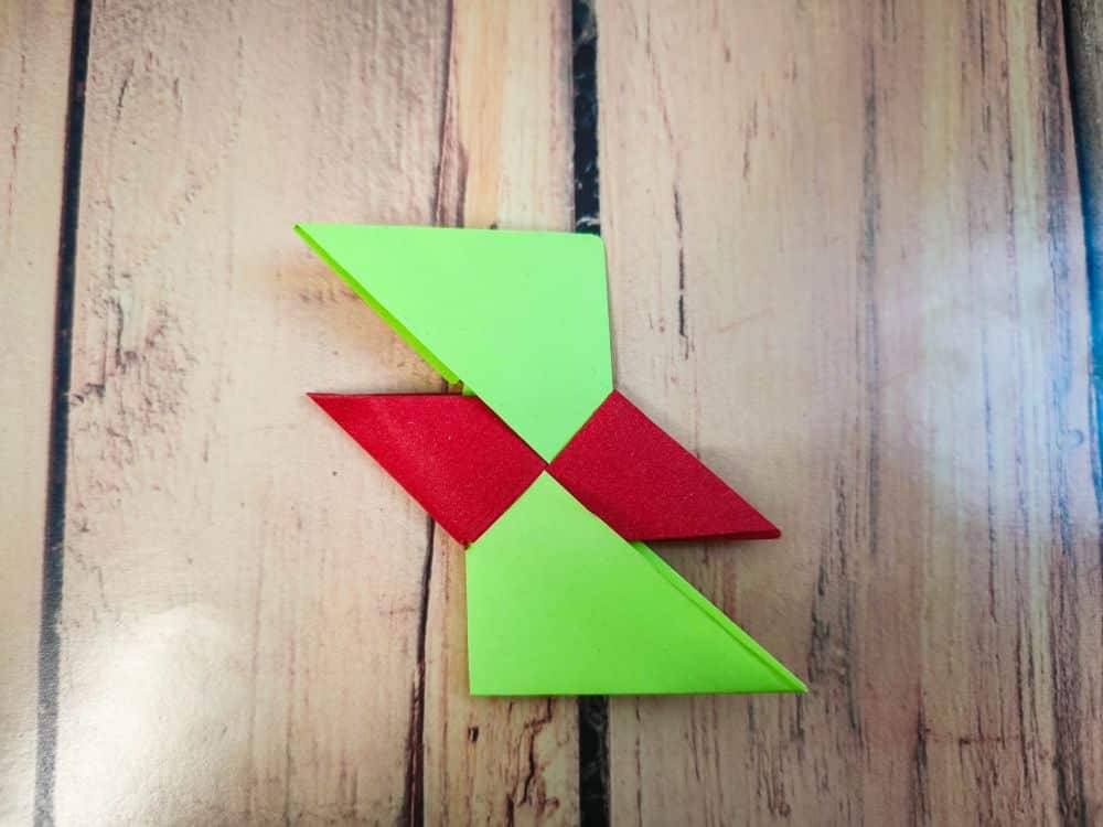 Eine geometrische Origami-Papierform aus zwei grünen Dreiecken und zwei roten Dreiecken, die in einem Zickzack-Muster angeordnet sind und auf einer Holzunterlage liegen.