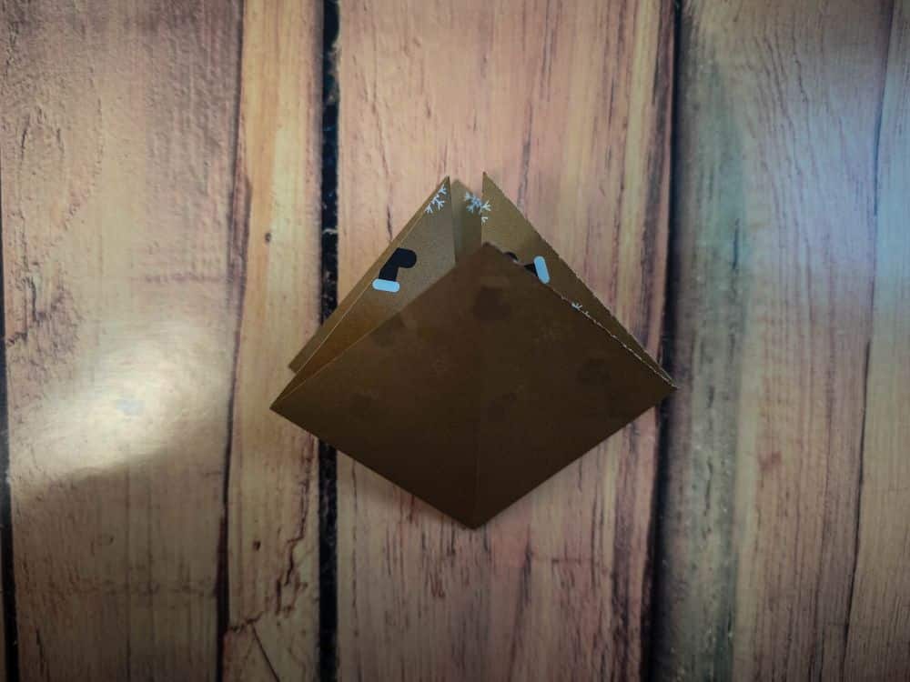 Ein gefaltetes Stück braunes Papier mit einem subtilen Schneeflockenmuster liegt auf einer hölzernen Oberfläche und erinnert an die Anfänge einer Origami-Kreation.