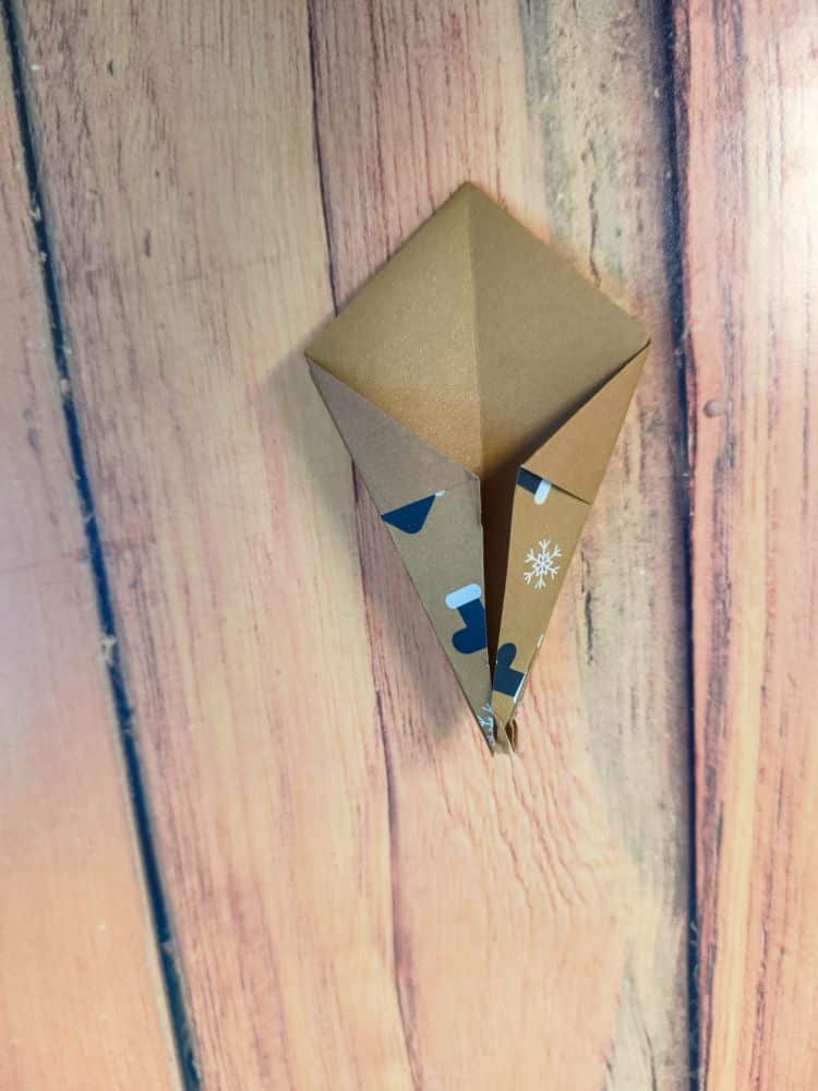 Ein braunes Origamipapier, das zu einem Drachen gefaltet und auf einer Seite mit blauen Strümpfen und einer weißen Schneeflocke verziert ist, ruht auf einer Holzfläche.