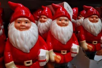 In einem Regal stehen dicht an dicht mehrere Weihnachtsmannfiguren aus Keramik mit roten Anzügen und weißen Bärten, wie geschaffen für Neujahrsfeiern. Einige befinden sich teilweise in Pappschachteln, alle mit rosigen Wangen und lächelnden Gesichtern.