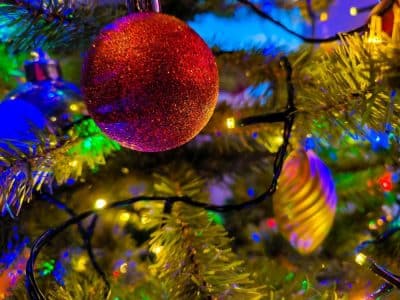 Nahaufnahme eines geschmückten Weihnachtsbaums mit einem roten glitzernden Ornament, bunte Lichterketten und verschwommene Ornamente im Hintergrund. Die festliche und helle Atmosphäre sagt "Frohe Weihnachten" - メリークリスマス!.