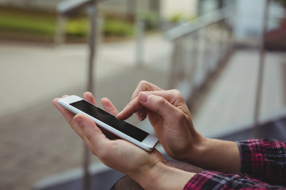 Eine Person, die ein Smartphone mit eSIM in einer Hand hält und mit der anderen Hand den Bildschirm berührt, sitzt im Freien in der Nähe eines Metallgeländers.