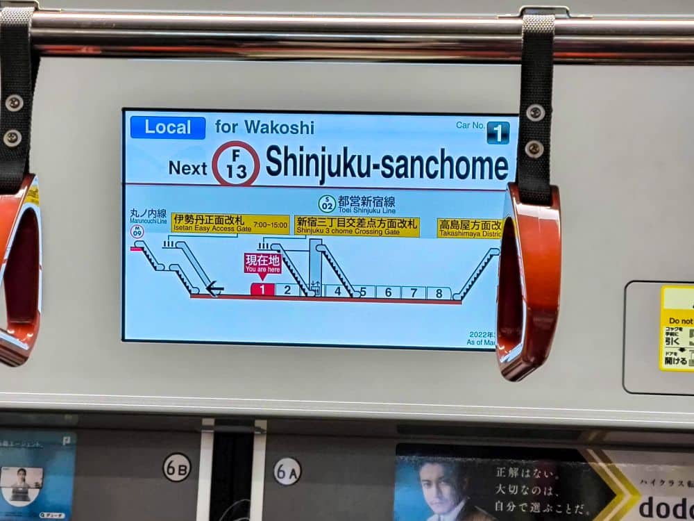 Auf einem Metro-Bildschirm wird eine Streckenkarte für die Fukutoshin-Linie der Tokioter Metro angezeigt. Die nächste Haltestelle ist Shinjuku-sanchome (F-13), mit japanischem und englischem Text, Stationsnummern und farbigen Umsteigelinien.