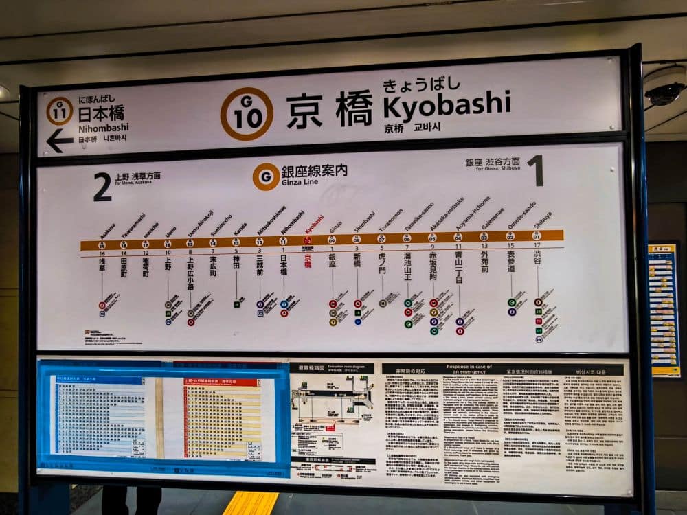 Ein Schild der U-Bahn-Station Kyobashi an der Ginza-Linie der Tokioter U-Bahn zeigt Stationsnamen, Streckenplan, Umsteigeverbindungen, Bahnsteignummern und Informationen in Japanisch und Englisch.