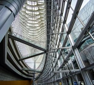 Innenansicht des Tokyo International Forum mit großen Glasfenstern, Metallträgern und einer hohen, geschwungenen Decke mit komplizierter architektonischer Gestaltung. Natürliches Licht durchflutet das geräumige, futuristische Atrium.