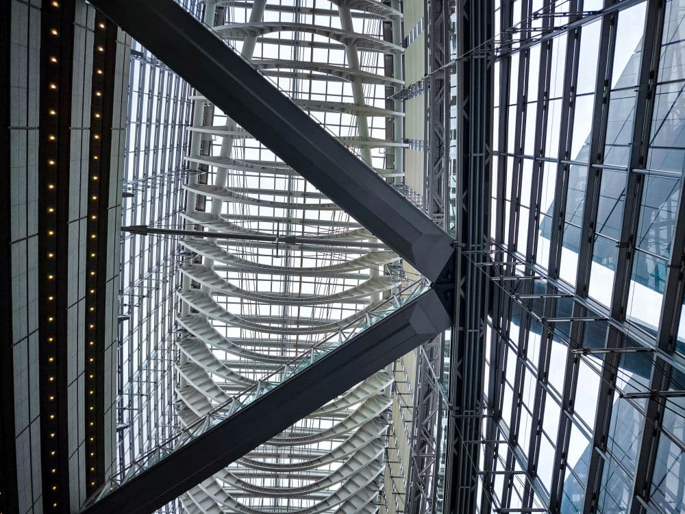 Innenansicht des Tokyo International Forum, eines modernen Gebäudes mit einer komplexen Stahl-Glas-Konstruktion mit sich kreuzenden Trägern, geschwungenen architektonischen Elementen und großen Fenstern, die das Tageslicht hereinlassen.