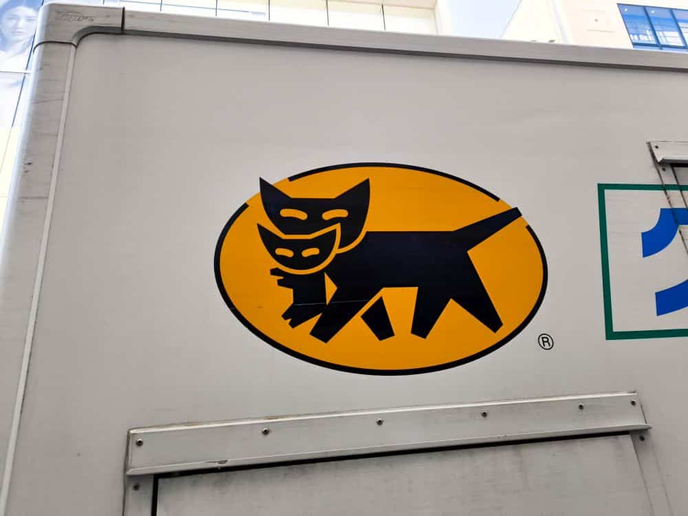 Das Takkyubin-Logo zeigt eine schwarze Katze, die ein schwarzes Kätzchen im Maul trägt, in einem gelben Oval, das auf der Seite eines weißen Lastwagens angebracht ist.